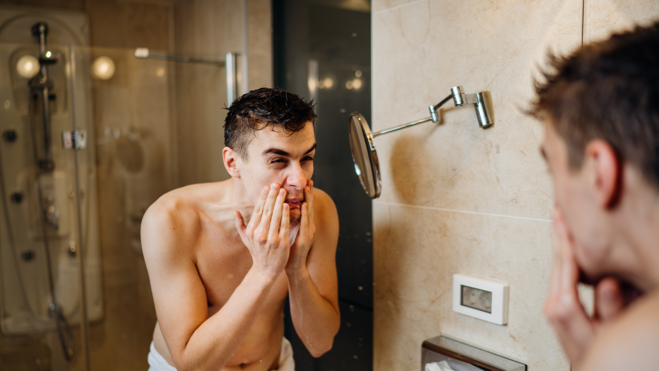 Man in mirror holding face in pain after shaving