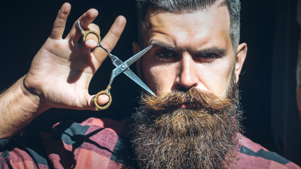 Man with beard holding scissors in hand lifted to his face